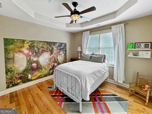 bedroom featuring ceiling fan, a tray ceiling, and wood-type flooring