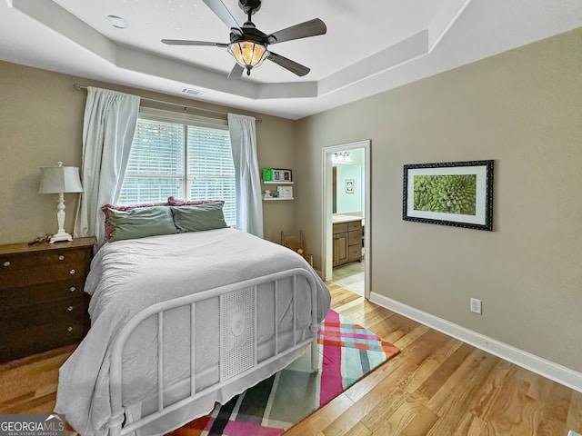 bedroom featuring connected bathroom, a tray ceiling, ceiling fan, and light hardwood / wood-style flooring