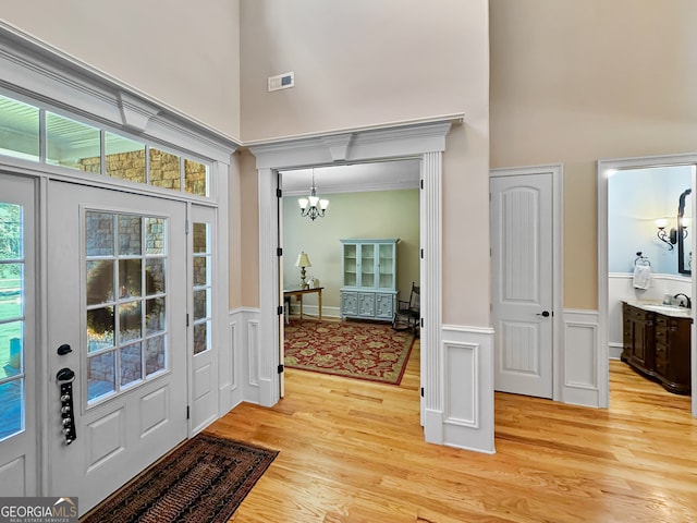 entryway featuring light wood-type flooring, a high ceiling, sink, and a notable chandelier