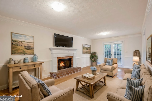 living room featuring french doors, a fireplace, ornamental molding, and light hardwood / wood-style flooring