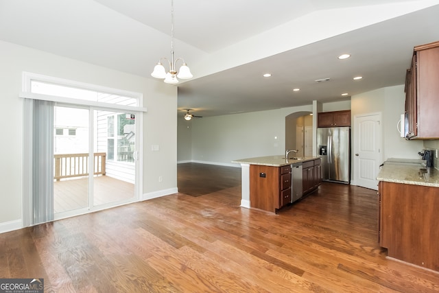 kitchen featuring an island with sink, hanging light fixtures, dark wood-type flooring, stainless steel appliances, and light stone countertops