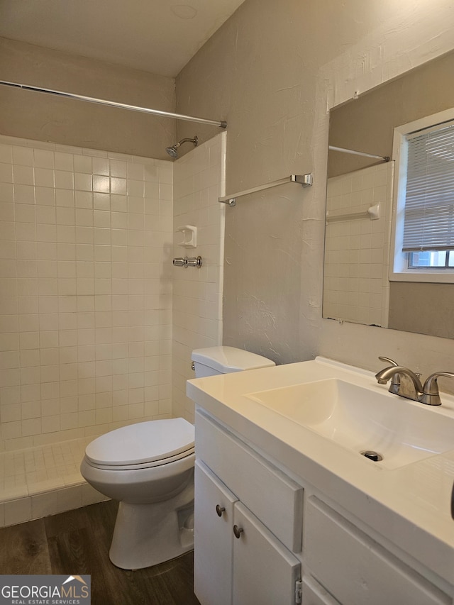 bathroom featuring wood-type flooring, vanity, toilet, and tiled shower