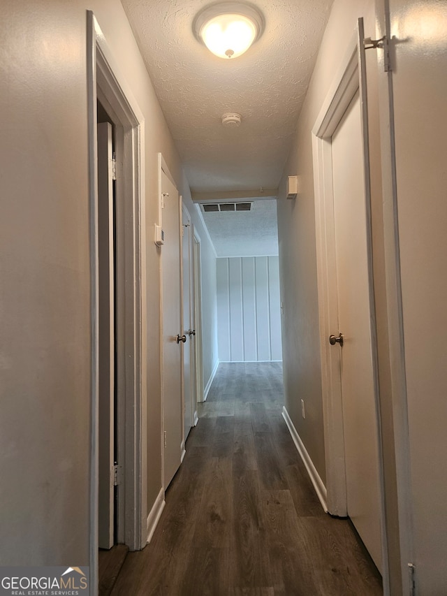 hallway with a textured ceiling and dark hardwood / wood-style flooring