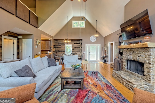 living room with wood-type flooring, a stone fireplace, a wealth of natural light, and high vaulted ceiling