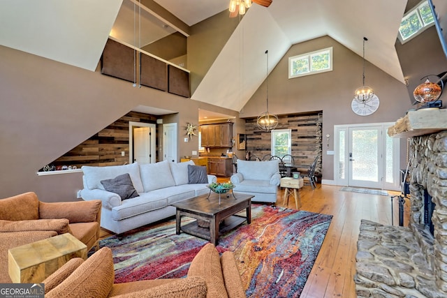 living room featuring ceiling fan with notable chandelier, wooden walls, hardwood / wood-style floors, and high vaulted ceiling