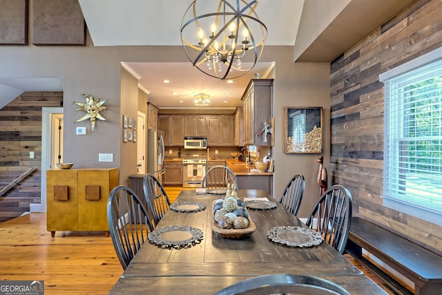 dining space with light hardwood / wood-style floors, wood walls, lofted ceiling, and a notable chandelier