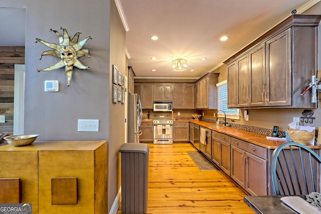 kitchen featuring sink, appliances with stainless steel finishes, ornamental molding, and light hardwood / wood-style flooring