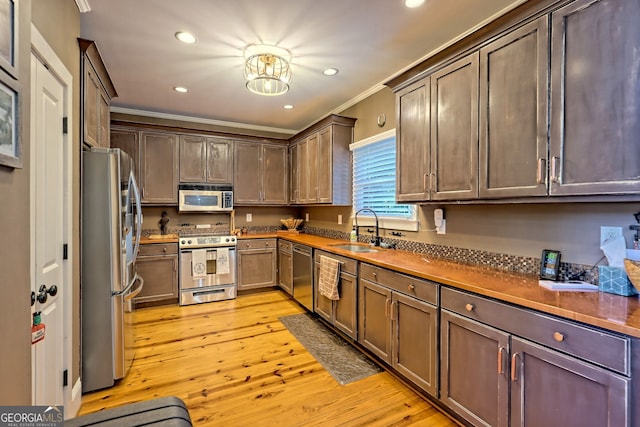 kitchen with dark brown cabinetry, sink, appliances with stainless steel finishes, crown molding, and light hardwood / wood-style floors