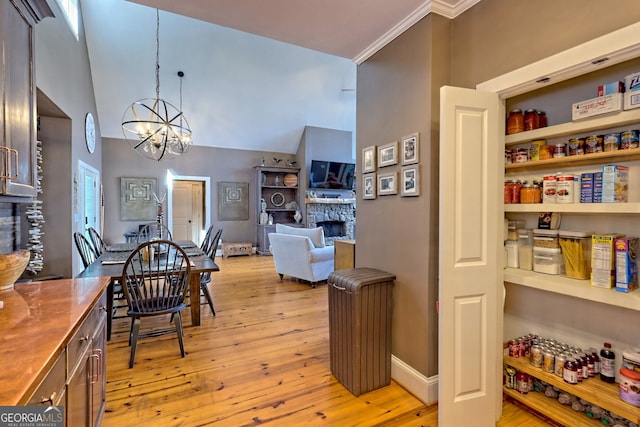 dining area with ornamental molding, a chandelier, high vaulted ceiling, a fireplace, and light wood-type flooring