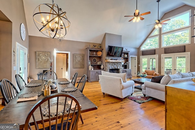 dining area featuring french doors, light hardwood / wood-style flooring, high vaulted ceiling, a fireplace, and ceiling fan with notable chandelier