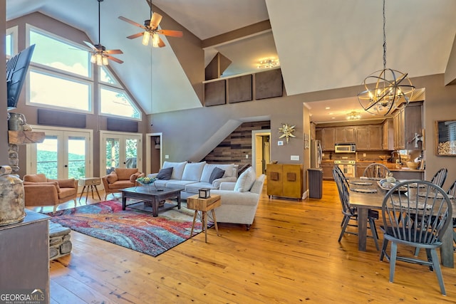 living room with high vaulted ceiling, light wood-type flooring, ceiling fan with notable chandelier, and french doors