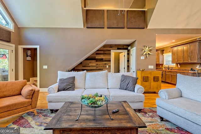 living room with high vaulted ceiling, wooden walls, light hardwood / wood-style floors, and sink