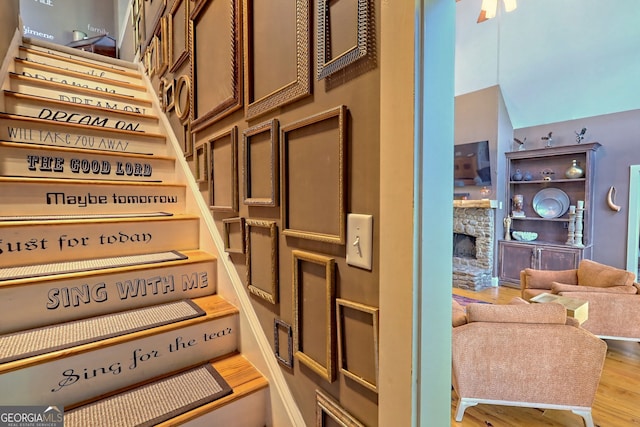 staircase featuring ceiling fan, hardwood / wood-style floors, and a stone fireplace