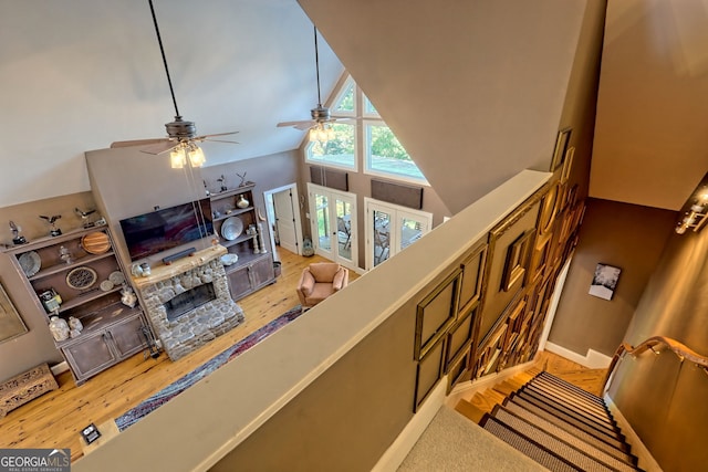 living room featuring high vaulted ceiling, ceiling fan, hardwood / wood-style floors, and a stone fireplace