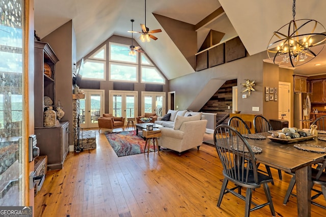 dining space featuring light hardwood / wood-style floors, ceiling fan with notable chandelier, high vaulted ceiling, wooden walls, and french doors