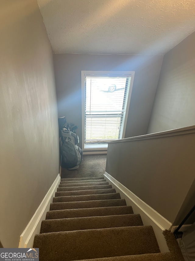 staircase featuring vaulted ceiling, a textured ceiling, and carpet flooring