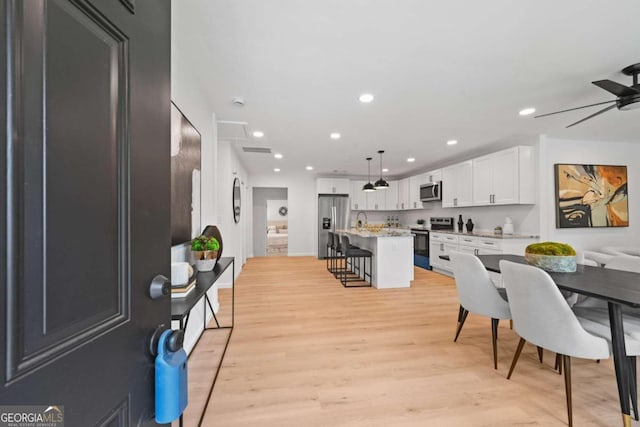 kitchen with white cabinetry, a breakfast bar area, stainless steel appliances, decorative light fixtures, and a kitchen island with sink