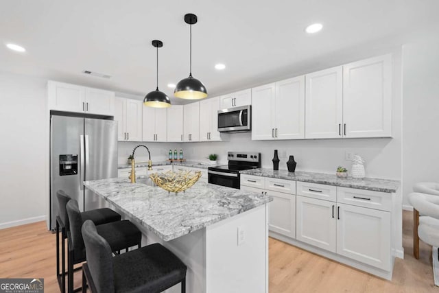 kitchen with appliances with stainless steel finishes, white cabinetry, light stone countertops, light hardwood / wood-style flooring, and a kitchen island with sink