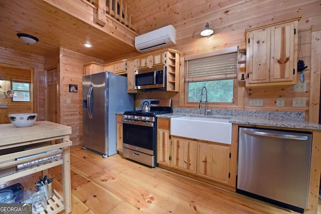 kitchen featuring appliances with stainless steel finishes, wood walls, light hardwood / wood-style flooring, a wall unit AC, and sink