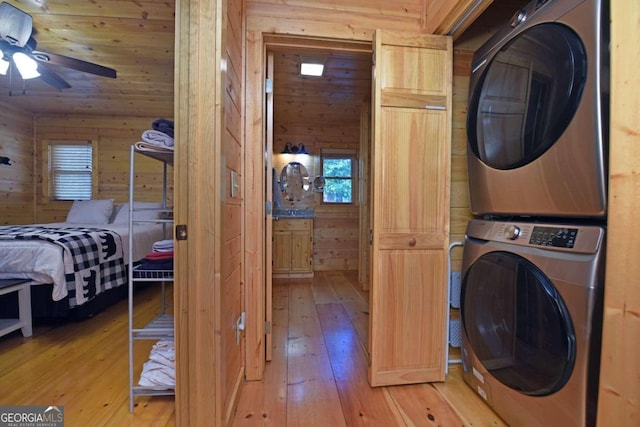 laundry room featuring ceiling fan, wooden walls, hardwood / wood-style floors, and stacked washer and dryer