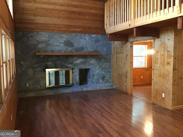 unfurnished living room featuring wood-type flooring, wooden ceiling, a stone fireplace, and wooden walls