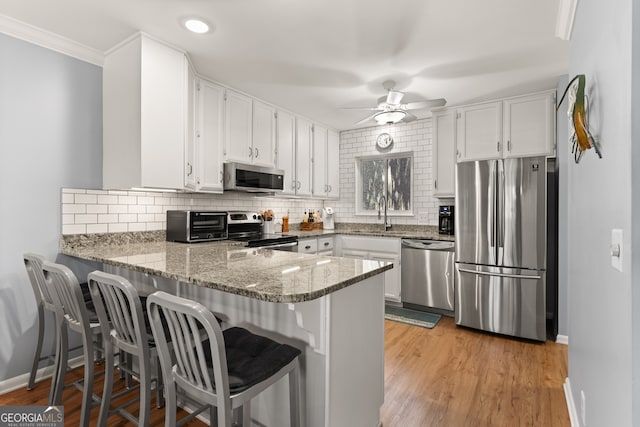 kitchen featuring ceiling fan, white cabinetry, appliances with stainless steel finishes, crown molding, and light hardwood / wood-style floors