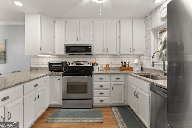 kitchen with appliances with stainless steel finishes, white cabinets, crown molding, light hardwood / wood-style flooring, and sink