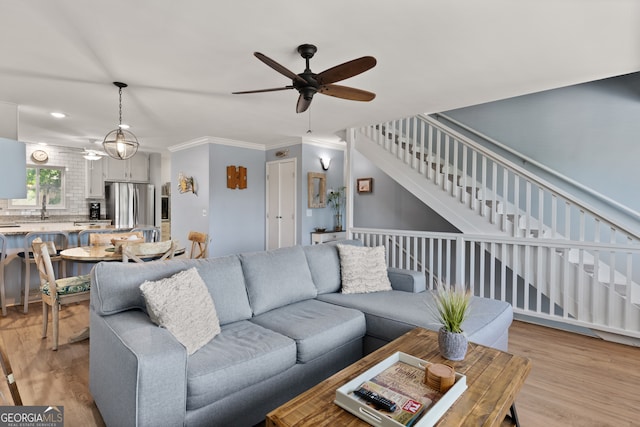 living room featuring light wood-type flooring, crown molding, sink, and ceiling fan