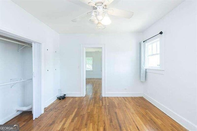 unfurnished bedroom with multiple windows, ceiling fan, a closet, and wood-type flooring