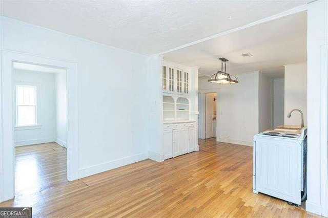 kitchen featuring washer / clothes dryer, white cabinetry, hanging light fixtures, and light hardwood / wood-style floors