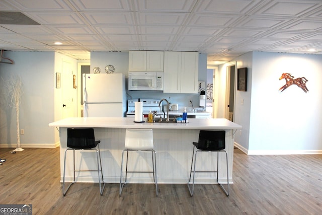 kitchen with hardwood / wood-style floors, a breakfast bar, white cabinetry, and white appliances