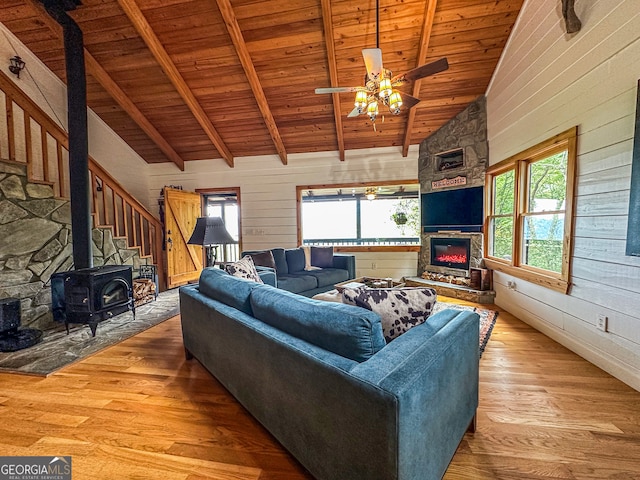 living room featuring wood ceiling, wood walls, beamed ceiling, ceiling fan, and a wood stove