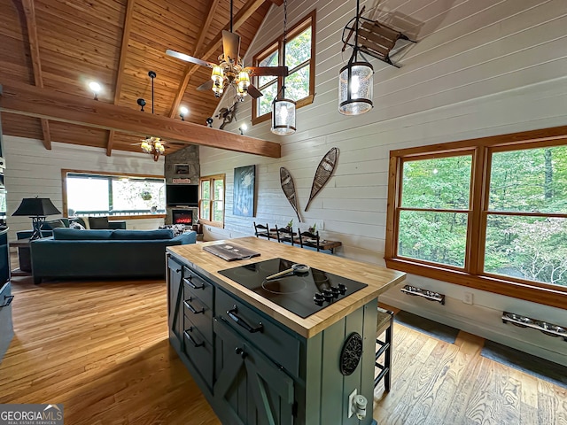 kitchen with decorative light fixtures, wood walls, black electric stovetop, ceiling fan, and beamed ceiling