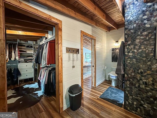 interior space featuring wood ceiling, wood walls, beamed ceiling, and toilet