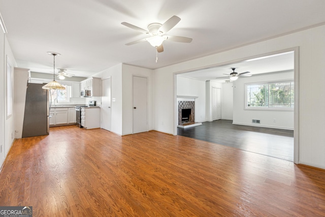 unfurnished living room featuring a brick fireplace, ceiling fan, and dark wood-type flooring