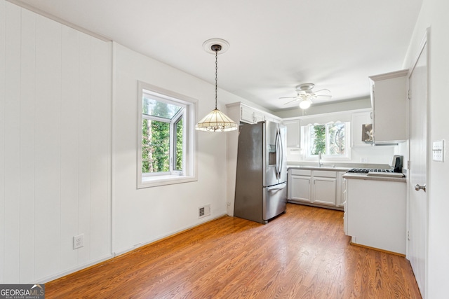 kitchen with white cabinetry, sink, hanging light fixtures, light hardwood / wood-style flooring, and appliances with stainless steel finishes