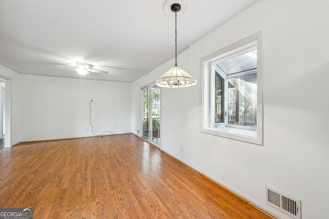 spare room with ceiling fan with notable chandelier and wood-type flooring