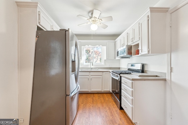 kitchen featuring stainless steel appliances, ceiling fan, sink, light hardwood / wood-style floors, and white cabinetry