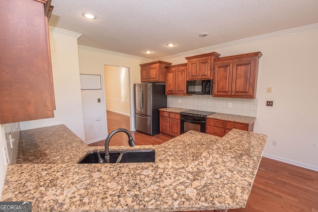 kitchen with sink, kitchen peninsula, black appliances, light stone countertops, and dark hardwood / wood-style flooring