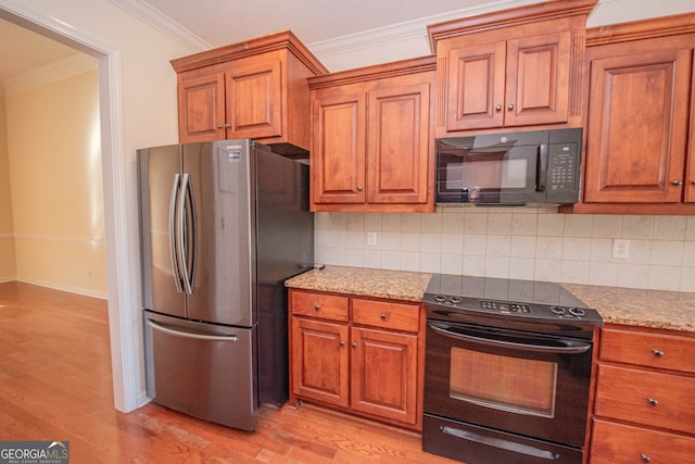 kitchen with light hardwood / wood-style floors, tasteful backsplash, crown molding, light stone counters, and black appliances