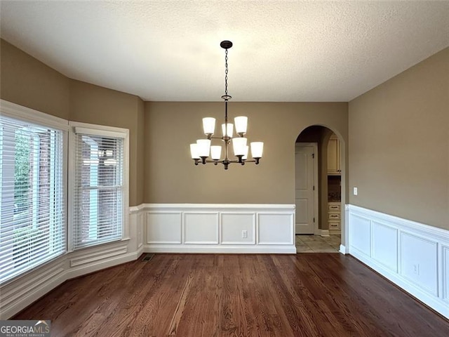 unfurnished dining area featuring a notable chandelier, dark hardwood / wood-style flooring, and a textured ceiling