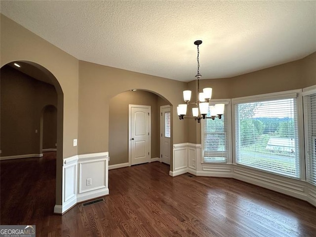 unfurnished dining area featuring a notable chandelier, dark hardwood / wood-style floors, and a textured ceiling