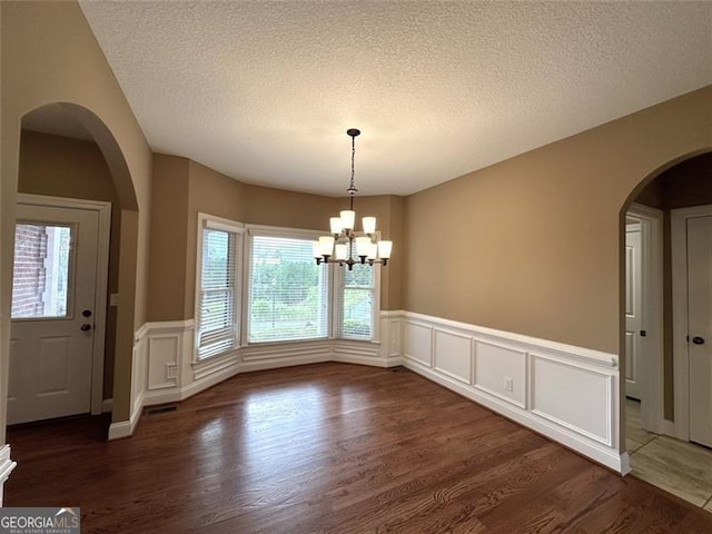 unfurnished dining area featuring an inviting chandelier, dark wood-type flooring, and a textured ceiling