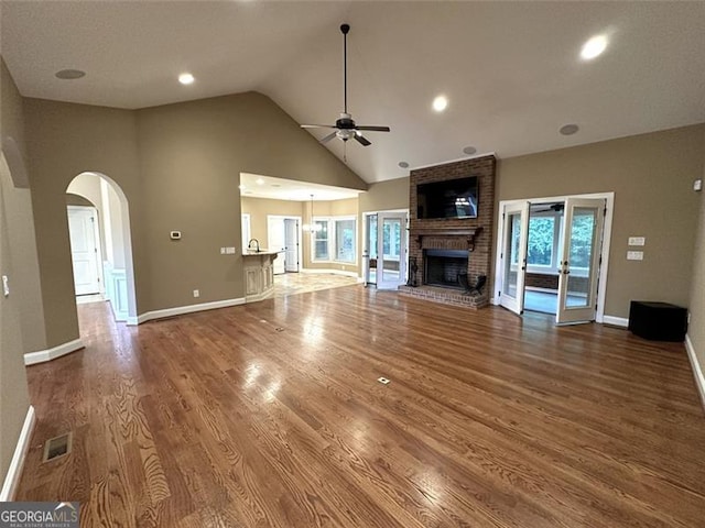 unfurnished living room with high vaulted ceiling, a brick fireplace, ceiling fan, french doors, and hardwood / wood-style floors