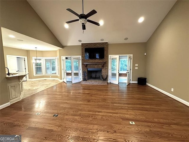 unfurnished living room with a fireplace, ceiling fan, dark wood-type flooring, and high vaulted ceiling