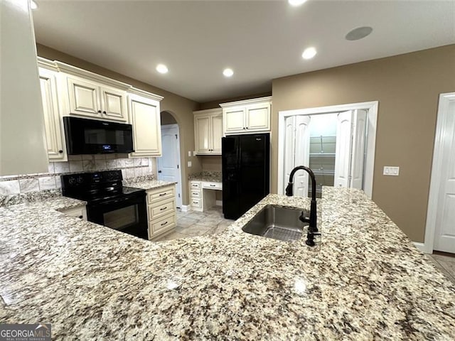 kitchen with sink, cream cabinets, backsplash, black appliances, and light stone countertops