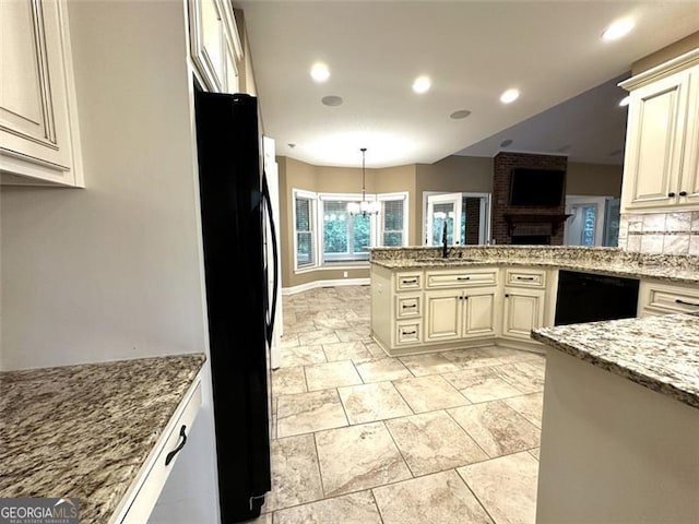 kitchen featuring light stone counters, hanging light fixtures, a brick fireplace, cream cabinetry, and black appliances