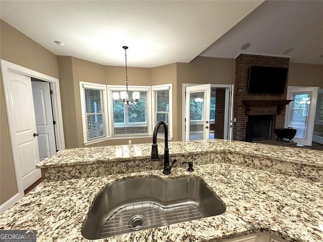 kitchen with light stone counters, hanging light fixtures, sink, an inviting chandelier, and a fireplace