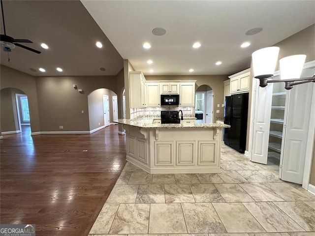 kitchen with tasteful backsplash, light hardwood / wood-style flooring, black appliances, a center island, and light stone countertops