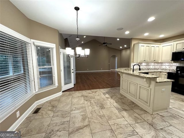 kitchen featuring vaulted ceiling, light stone countertops, black appliances, decorative light fixtures, and a center island with sink